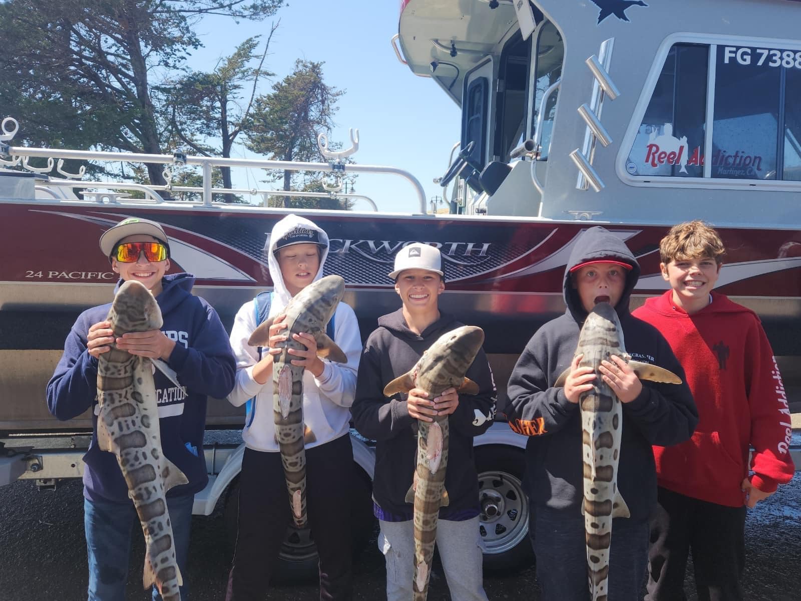 Five kids each holding a leopard shark beside the Reel Addiction boat