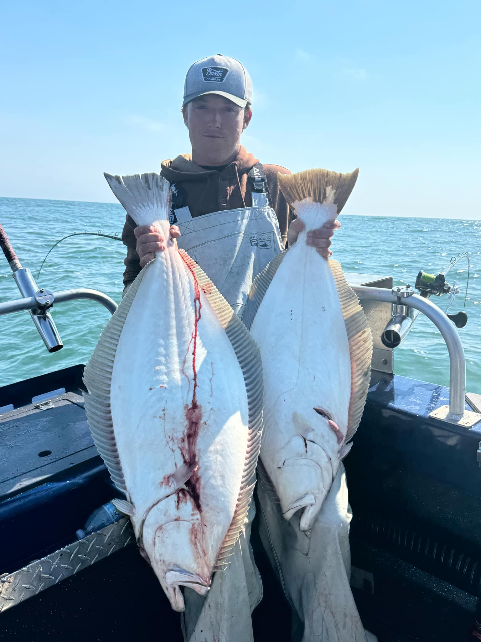 A young angler holding two California halibut on the boat