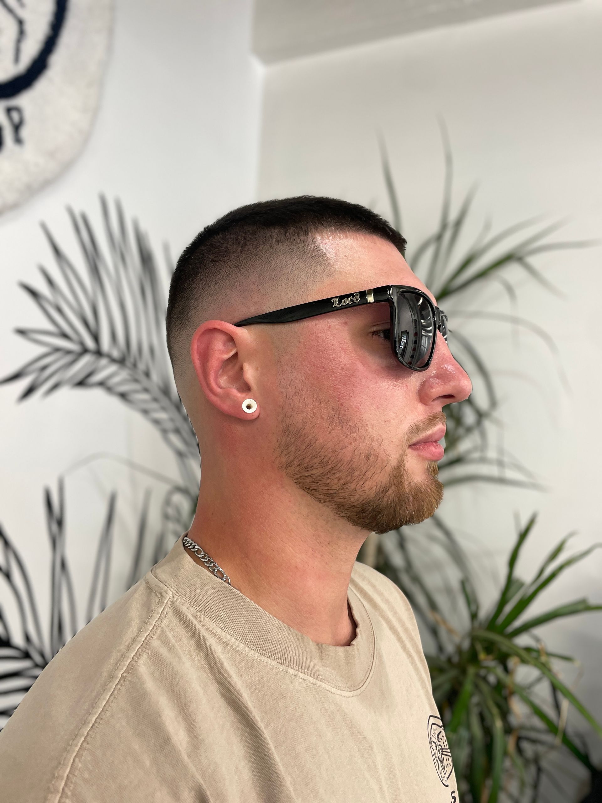 Young man with fresh fade haircut wearing Locs sunglasses inside a barbershop