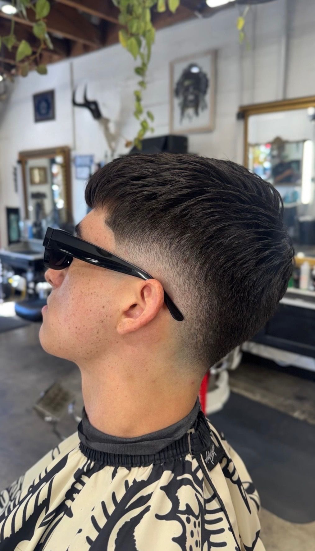 Man with fresh taper fade haircut sitting in barbershop chair wearing sunglasses