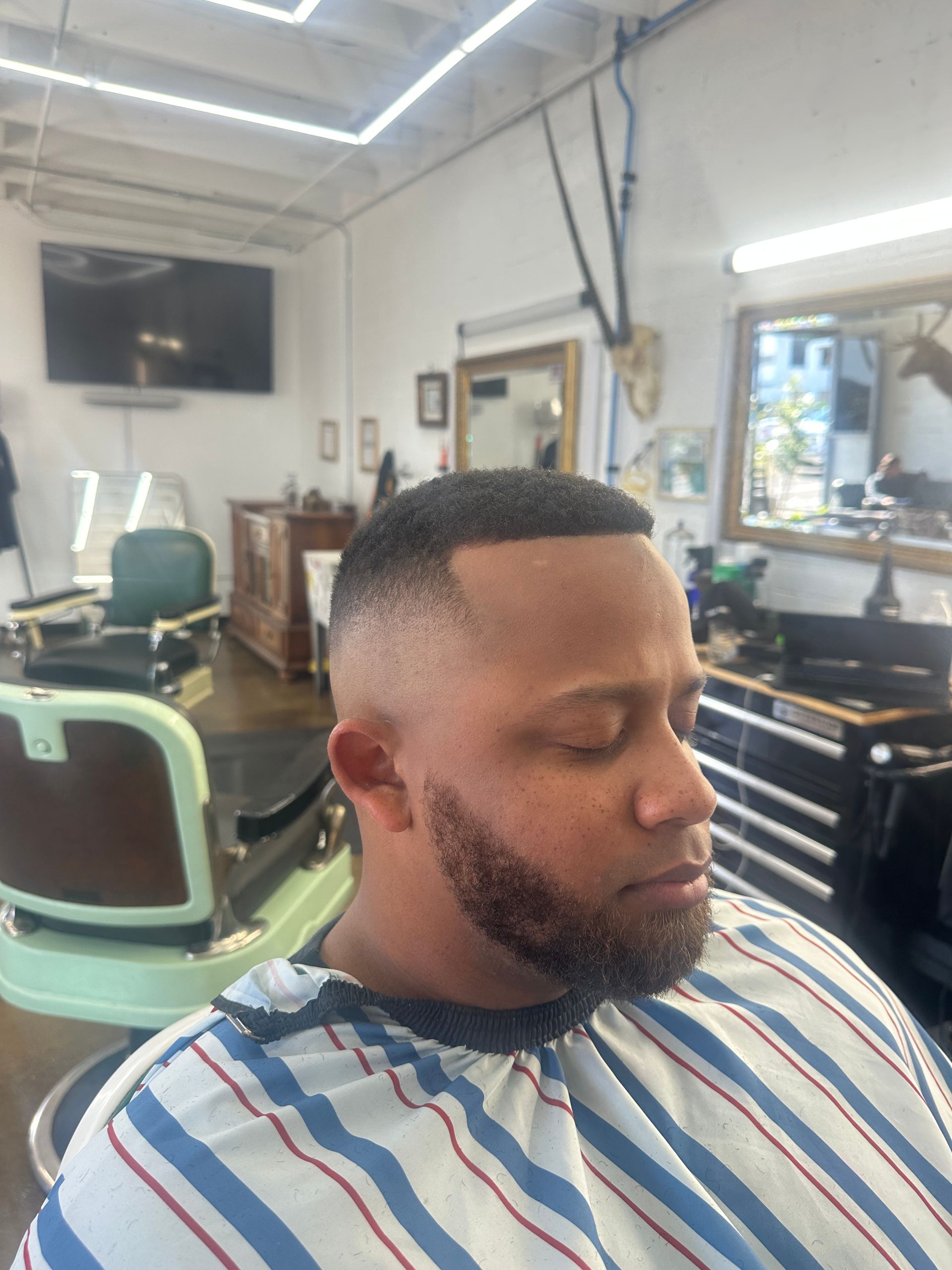 Man wearing barber cape sits in barbershop chair after fresh fade haircut