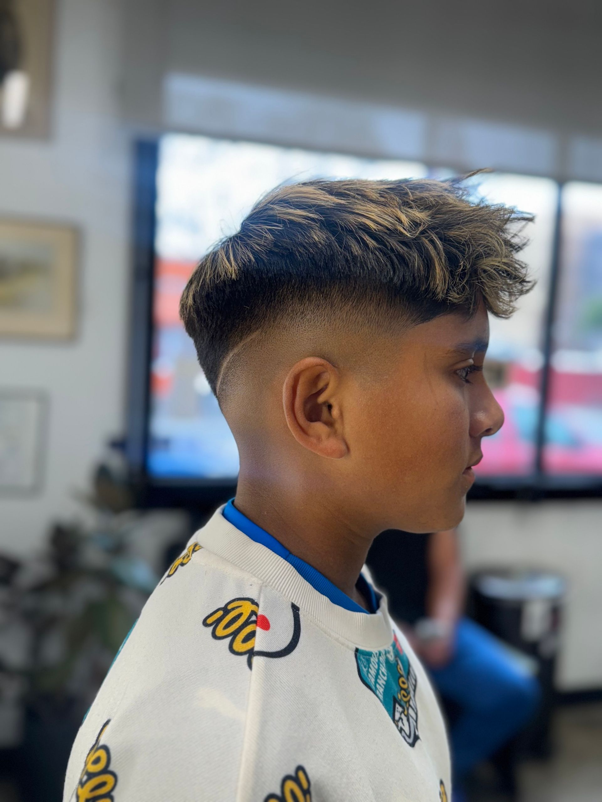 Young boy with a fresh fade haircut and blonde highlights at a barbershop