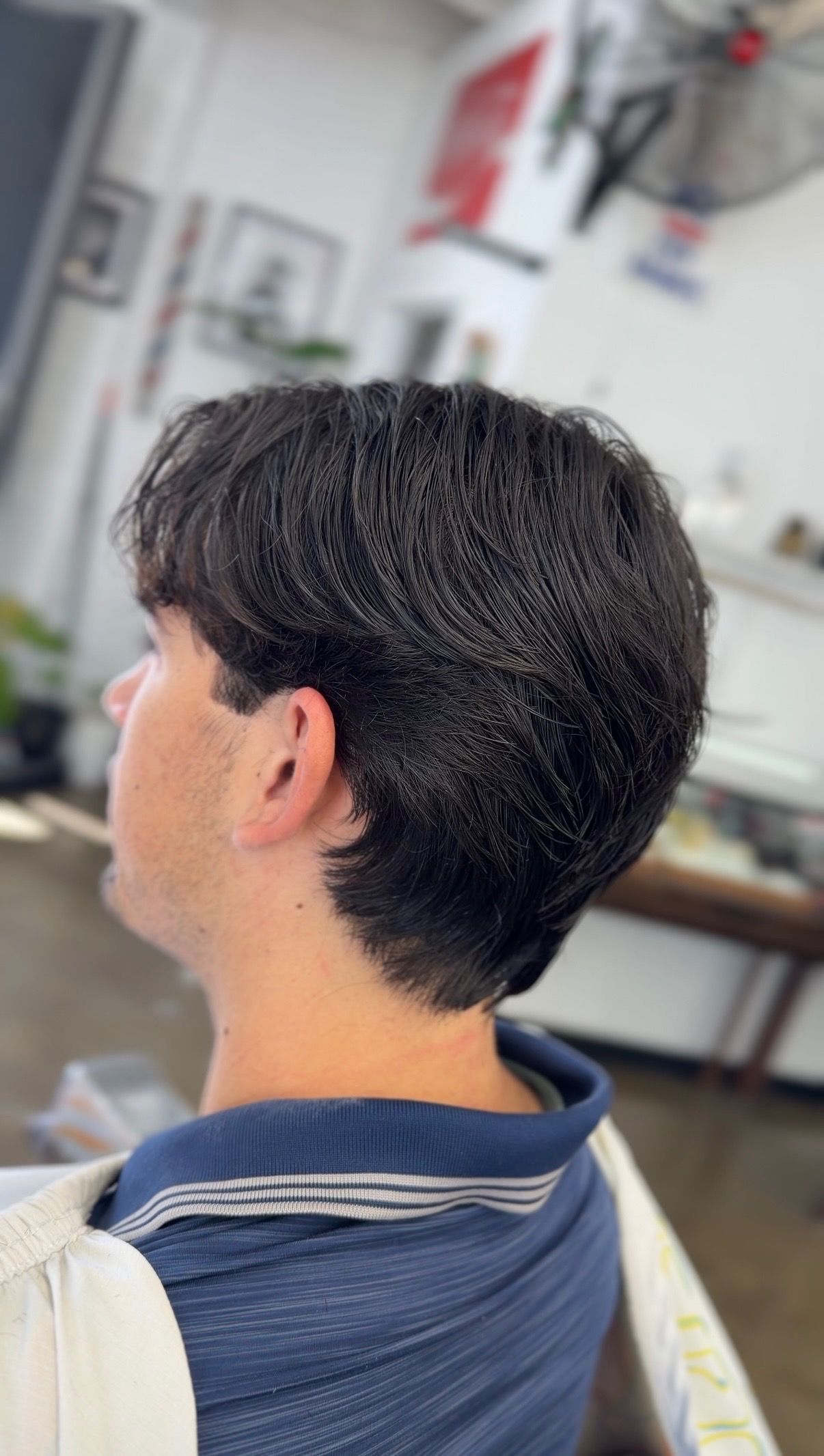 Man with fresh dark textured haircut seen from behind inside a barbershop