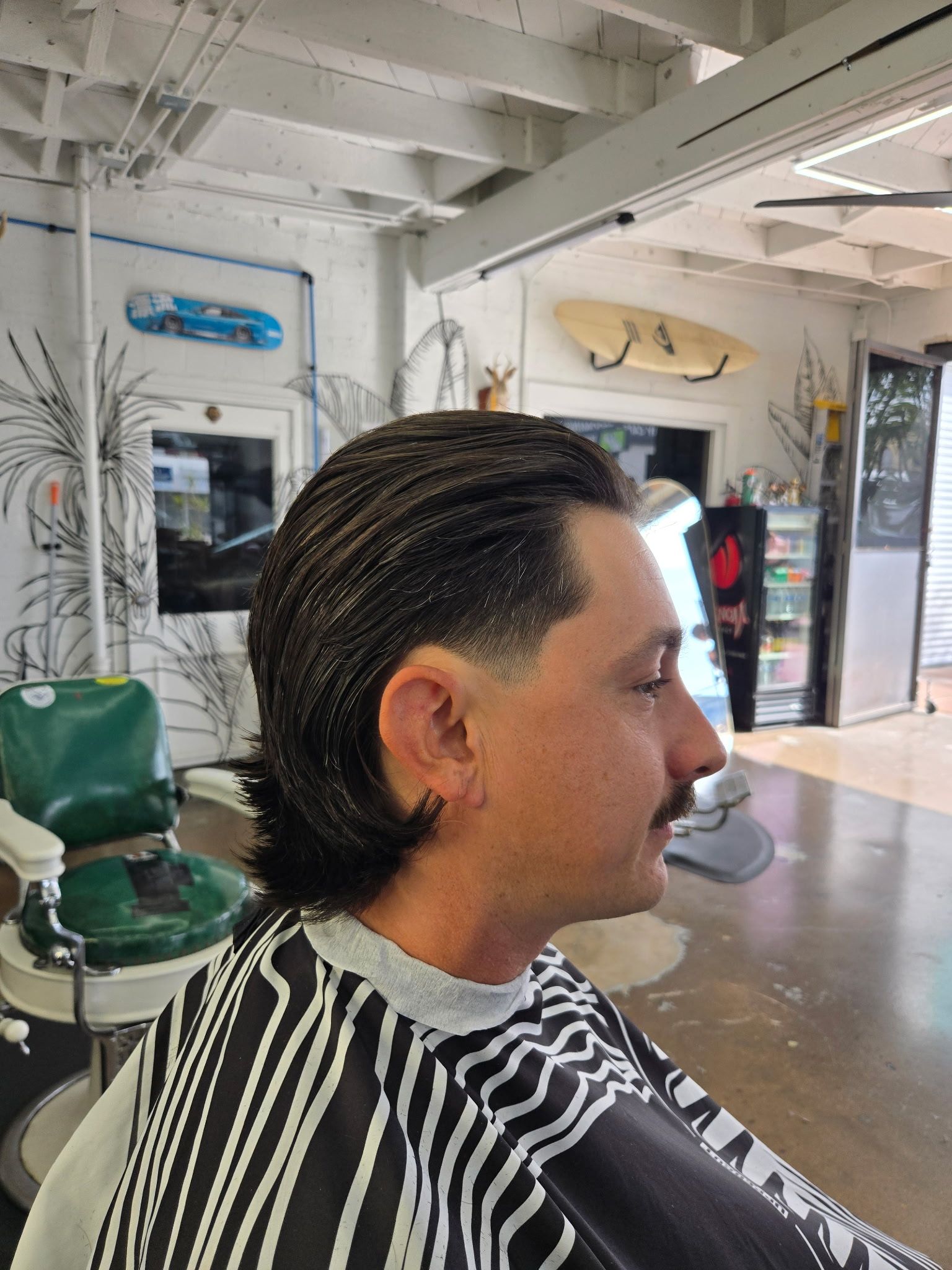 Man with slicked-back mullet and mustache sitting in barbershop chair