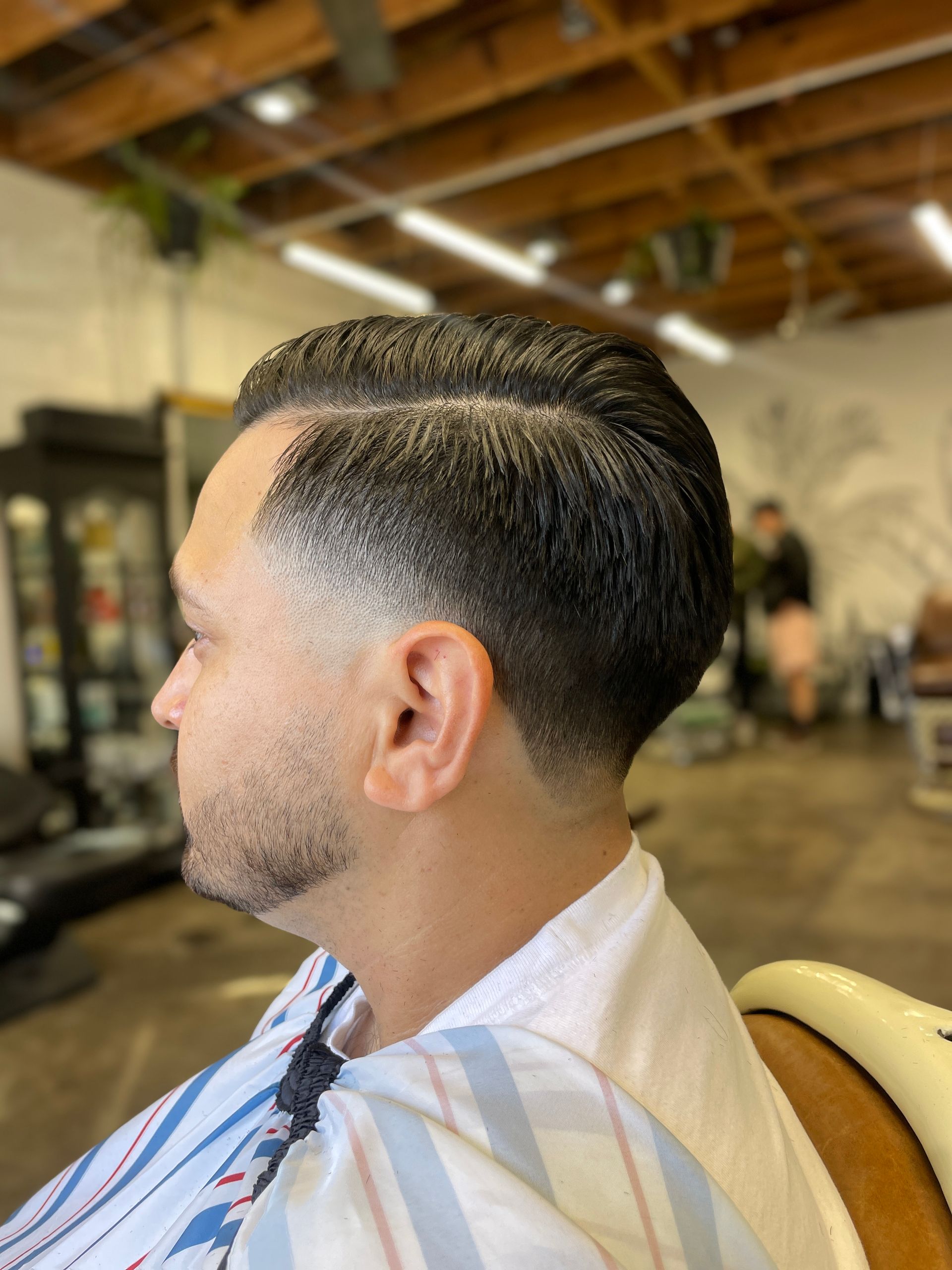 Man with slick back fade haircut sitting in barber chair at barbershop