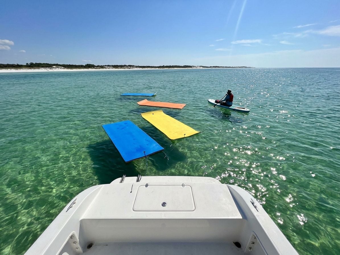 Floating lily pads and a paddleboarder in clear emerald water off the stern of a boat