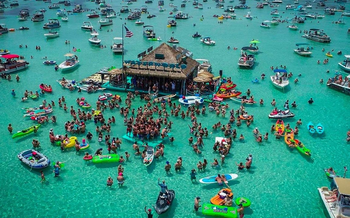 Aerial view of the Crab Island sandbar with the floating bar and boats anchored in emerald water